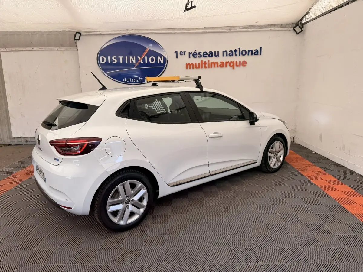 Renault Clio Business E-Tech hybride blanc vue 3/4 arrière droit en intérieur avec toit équipé d'une galerie.
