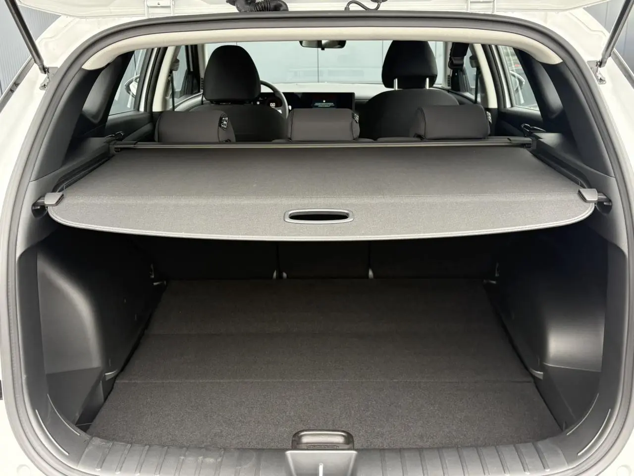 Coffre ouvert vu de l'arrière d'un Hyundai Tucson blanc Atlas 2026 avec cache-bagages déployé et intérieur noir.