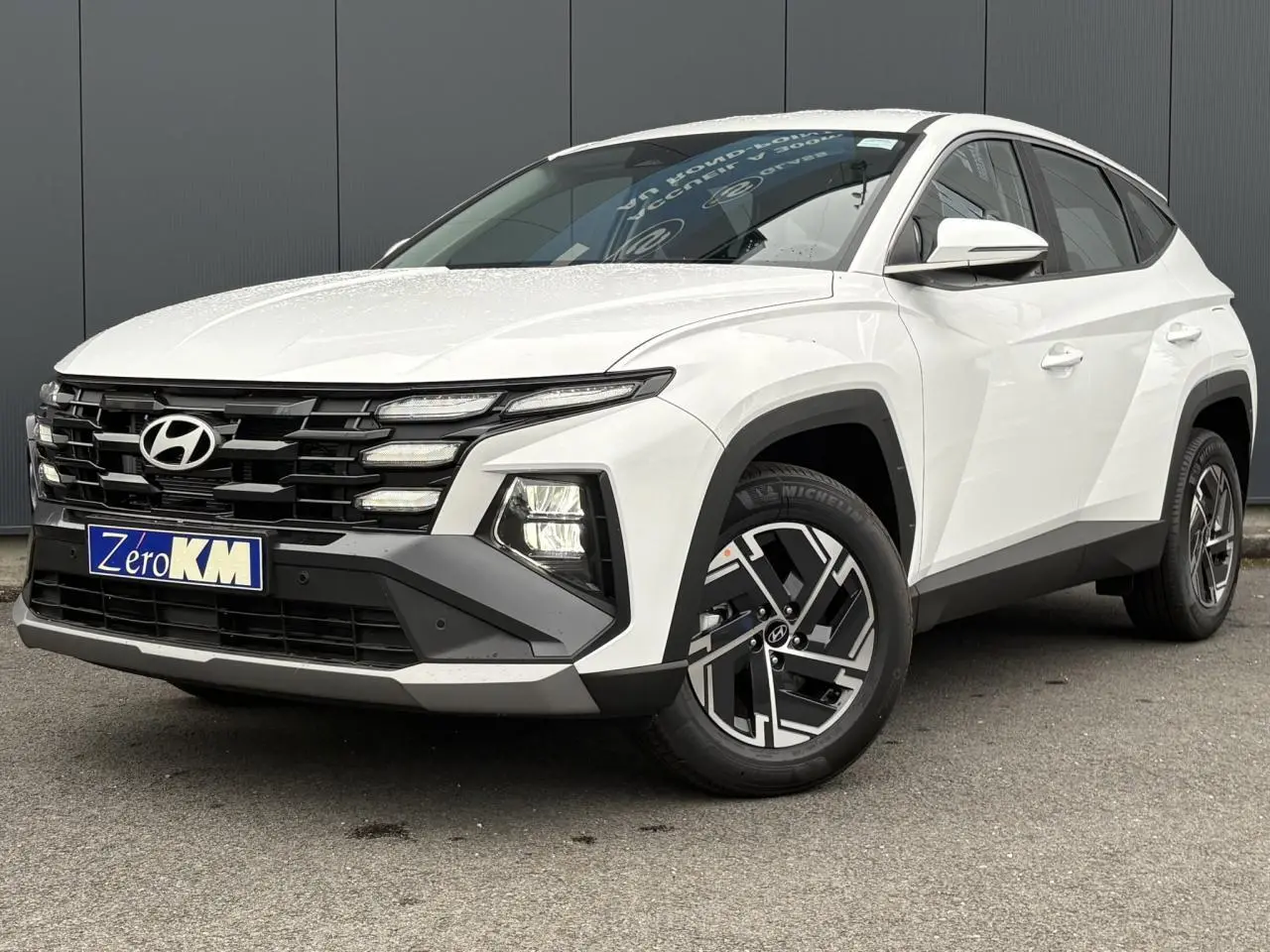 Hyundai Tucson blanc Atlas en 3/4 avant droit, avec calandre noire et jantes alliage 17 pouces distinctives.