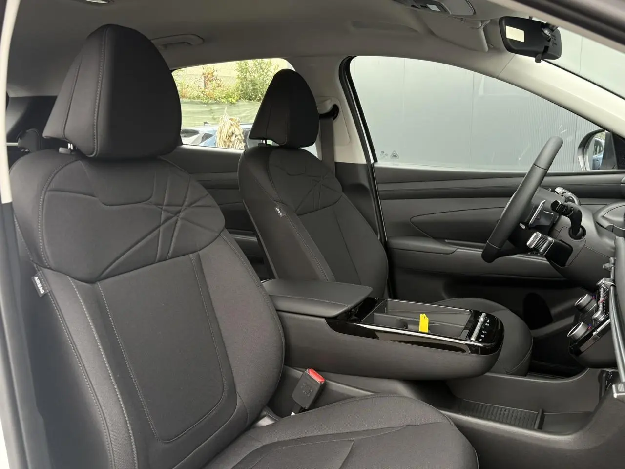 Vue intérieure côté conducteur du Hyundai Tucson 2026, sièges tissu noir et console centrale avec accoudoir.