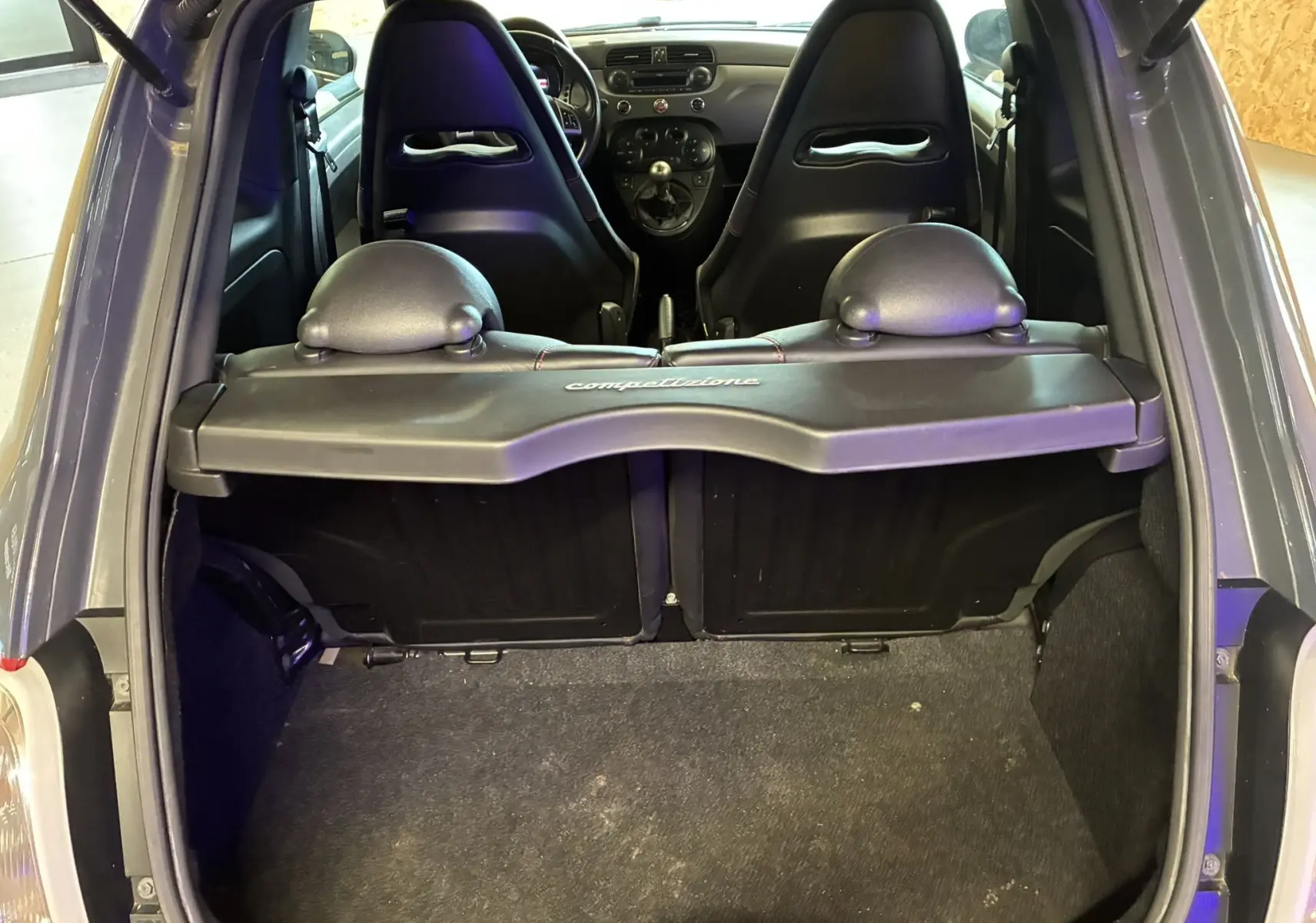 Vue arrière intérieure du coffre de l'Abarth 500 rouge 2016, avec sièges baquets et tablette "competizione" visible.