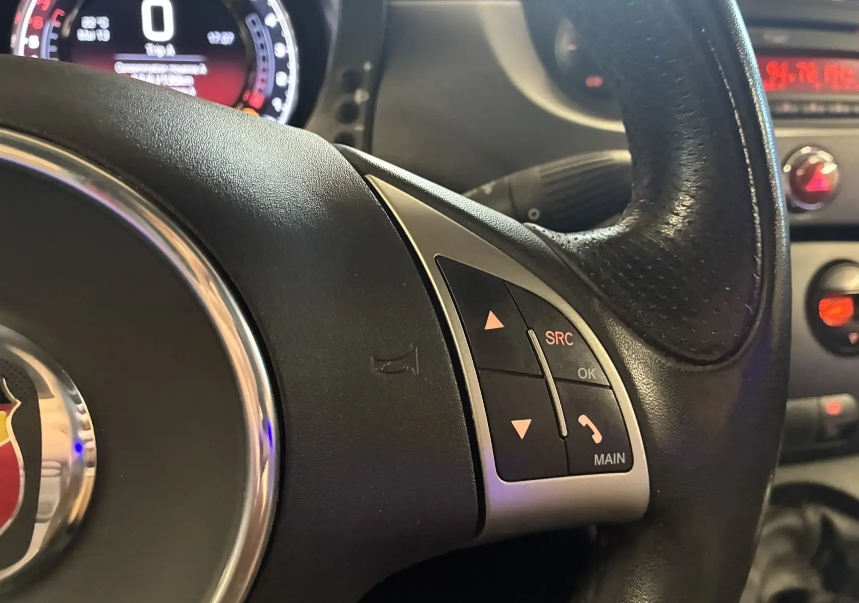 Gros plan sur le volant en cuir de l'Abarth 500 2016, avec commandes audio et tableau de bord partiellement visible.