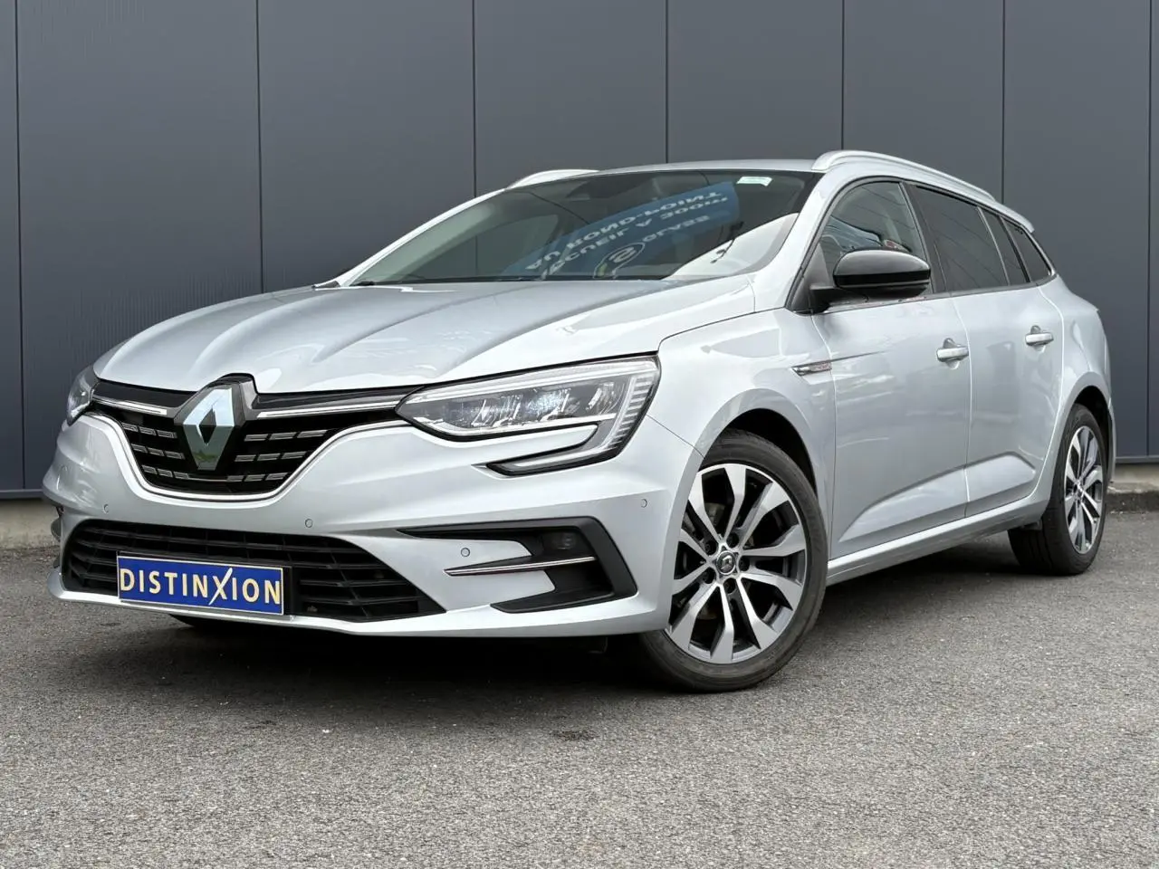 Renault Mégane Break gris clair vue 3/4 avant droit, avec jantes alliage et calandre noire distinctive.