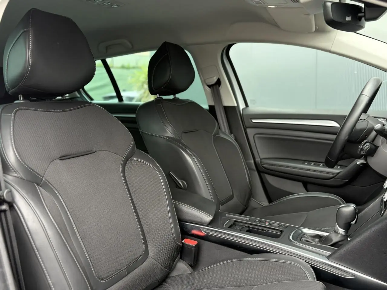 Vue intérieure côté conducteur et passager avant de la Renault Mégane Break 2024 avec sellerie mixte similicuir et tissu carbone.