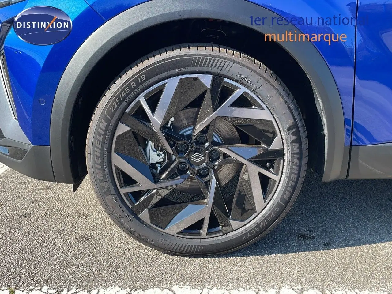 Gros plan sur la roue avant gauche du Renault Captur bleu Iron Metal avec jante alliage noire au design géométrique.