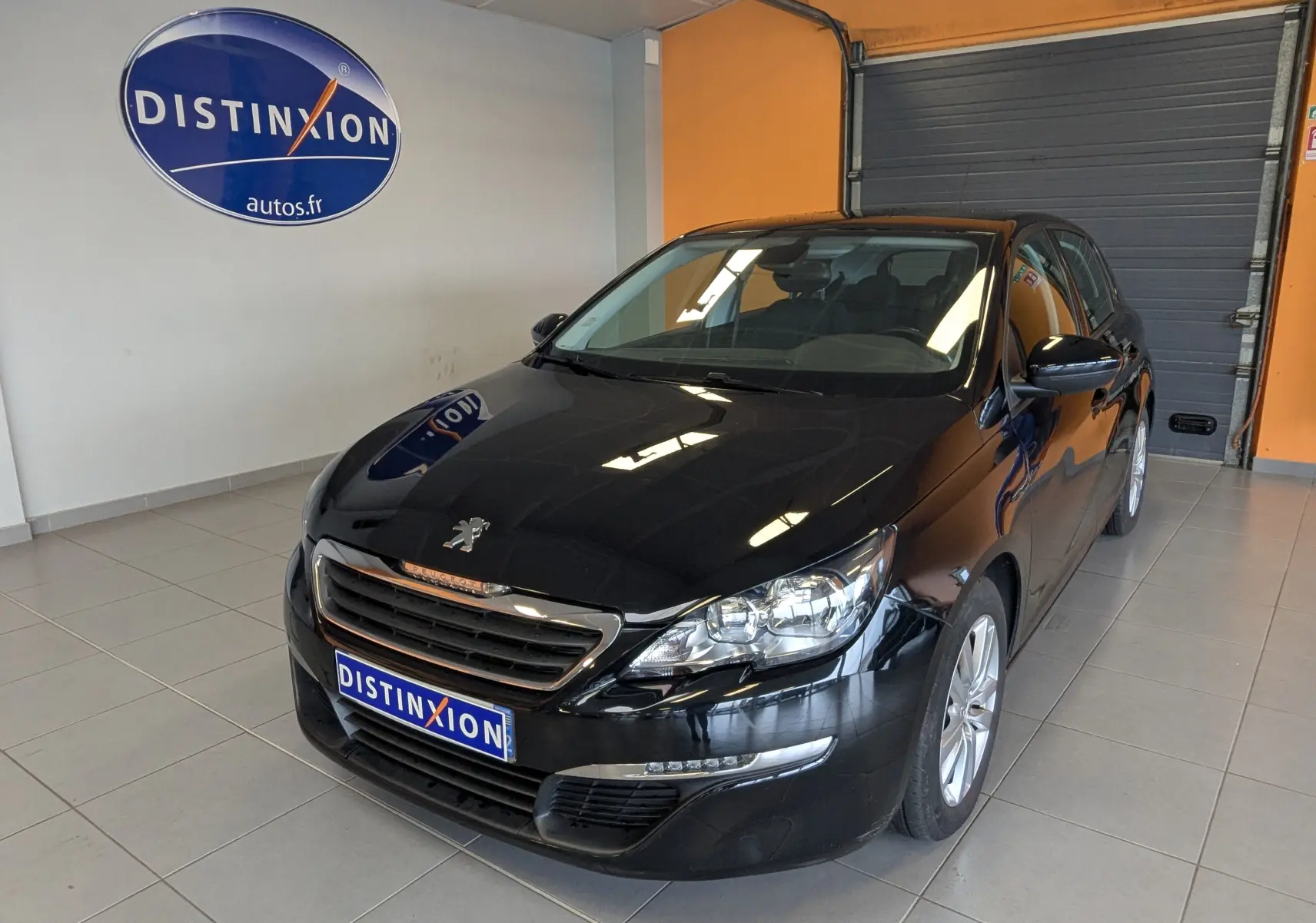 Peugeot 308 noire vue en 3/4 avant droit dans un showroom avec logo Distinxion en arrière-plan.