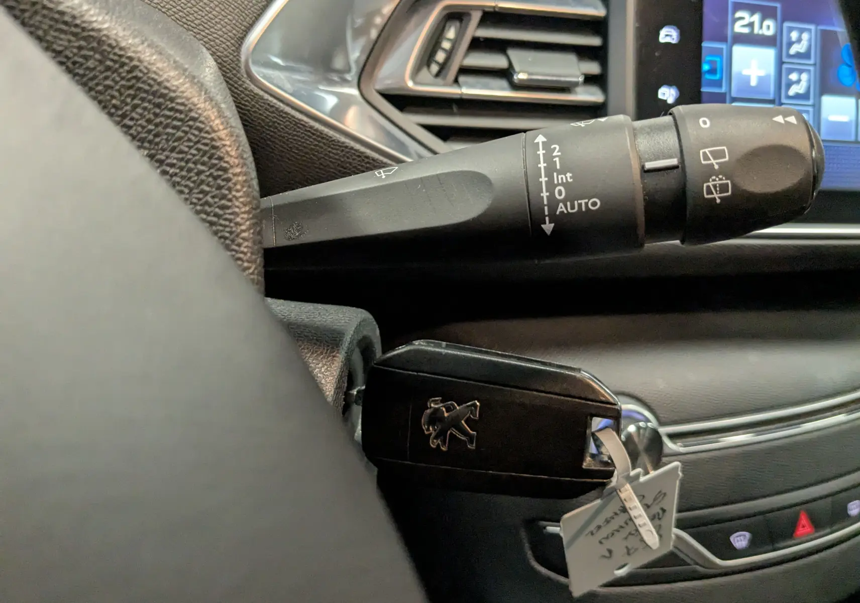 Gros plan sur la clé noire Peugeot insérée près du commodo d’essuie-glace, avec partie du tableau de bord et écran tactile visible.