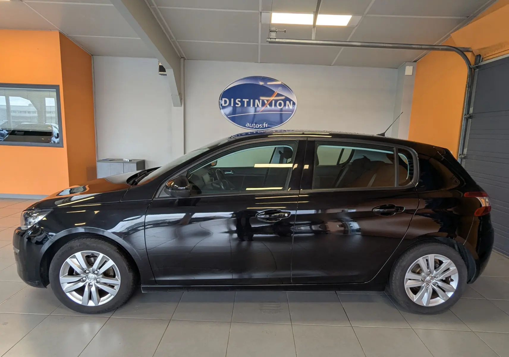 Profil côté gauche d'une Peugeot 308 noire 5 portes, version 1.2 PureTech 110 Style, en intérieur showroom.