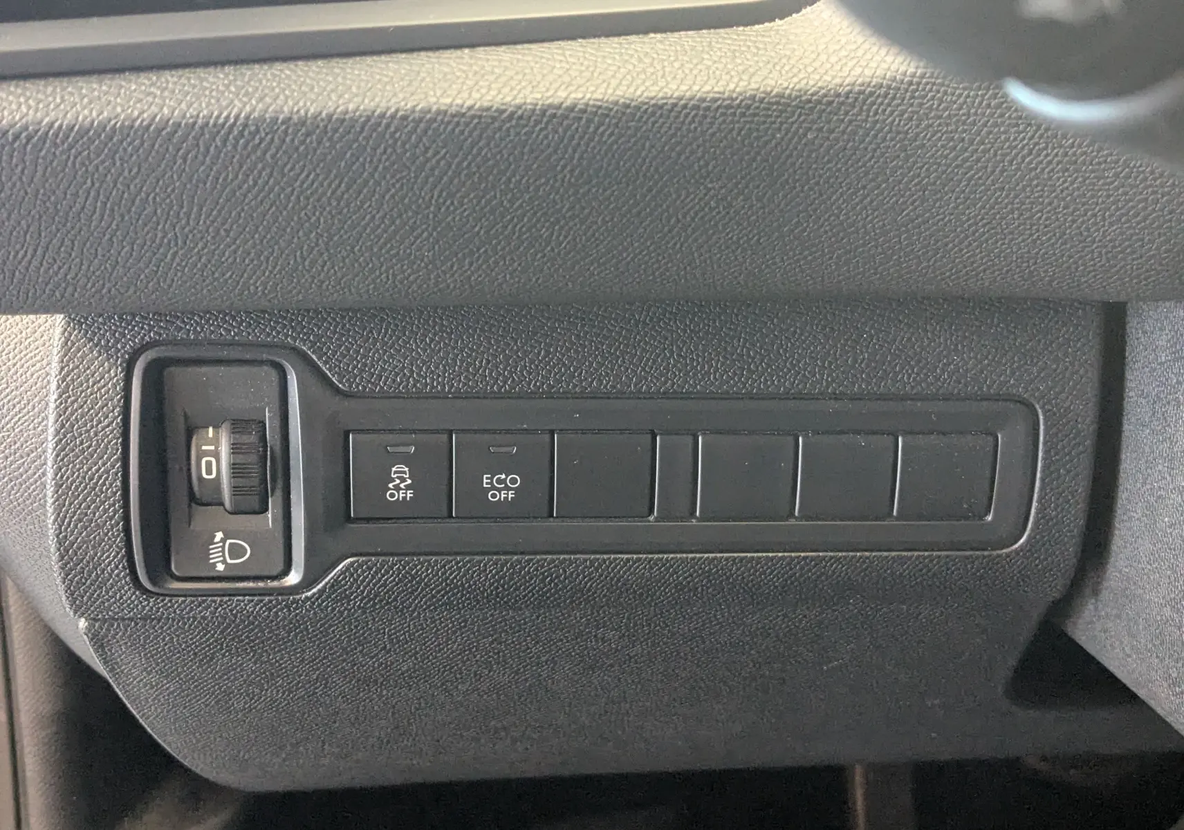 Vue rapprochée des commandes de réglage des phares et des fonctions ESP et ECO sur la Peugeot 308 noire 2017.