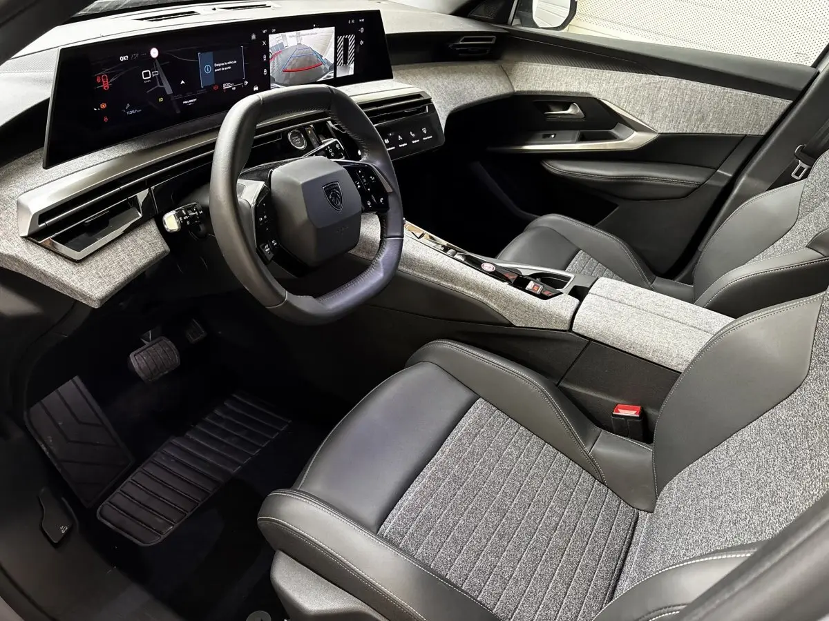 Vue intérieure côté conducteur du Peugeot 5008 2025, avec tableau de bord numérique et sièges gris clair tissu et cuir.