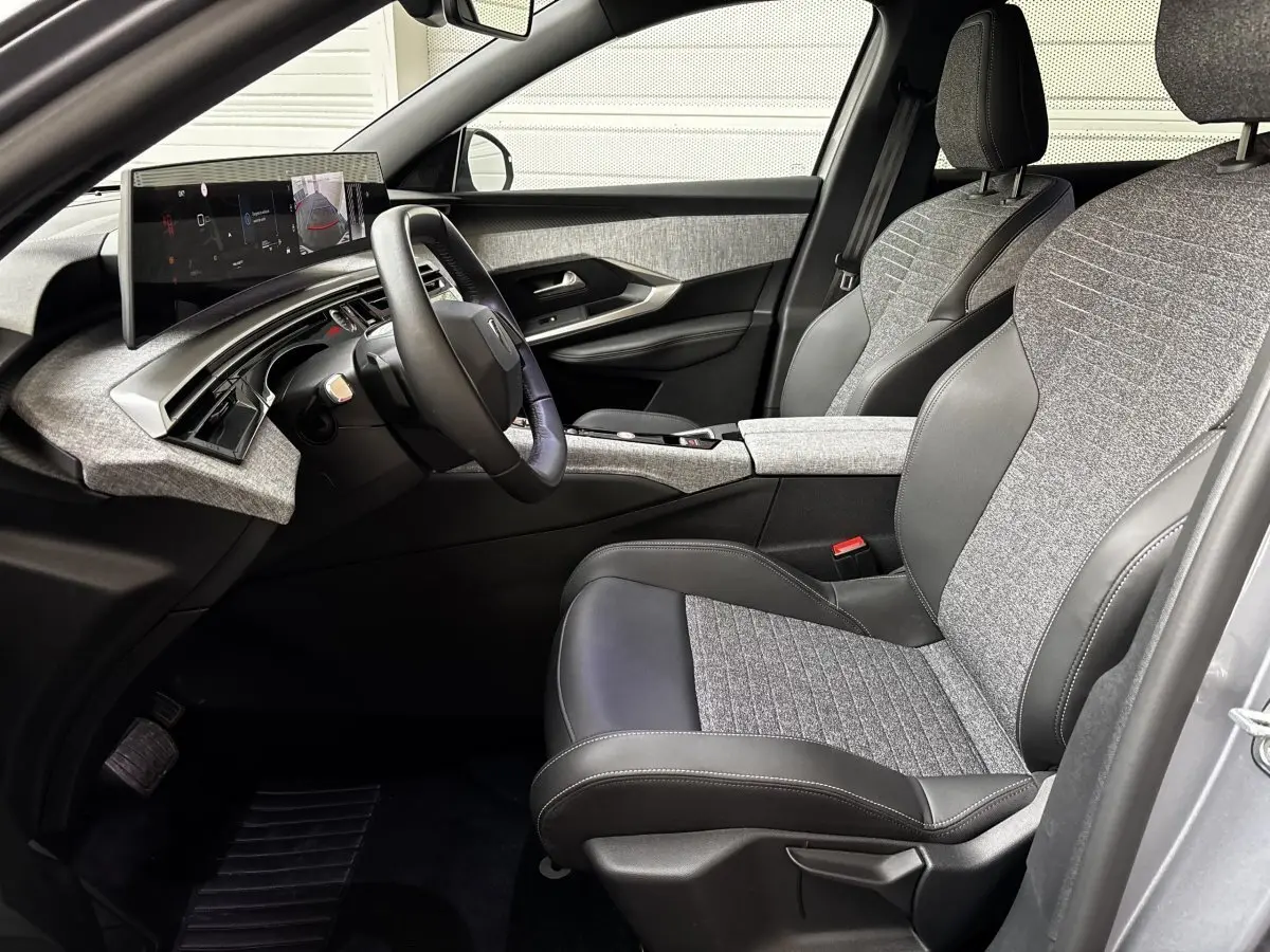 Vue intérieure côté conducteur de la Peugeot 5008 1.2 Hybrid 136 GT avec sièges tissu gris et cuir noir, tableau de bord moderne.