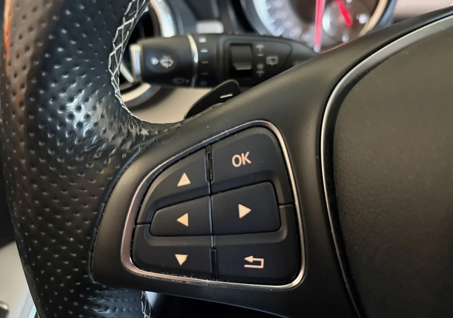 Gros plan sur les commandes multifonctions noires du volant cuir perforé d’une Mercedes GLA 200D Business gris de 2015.