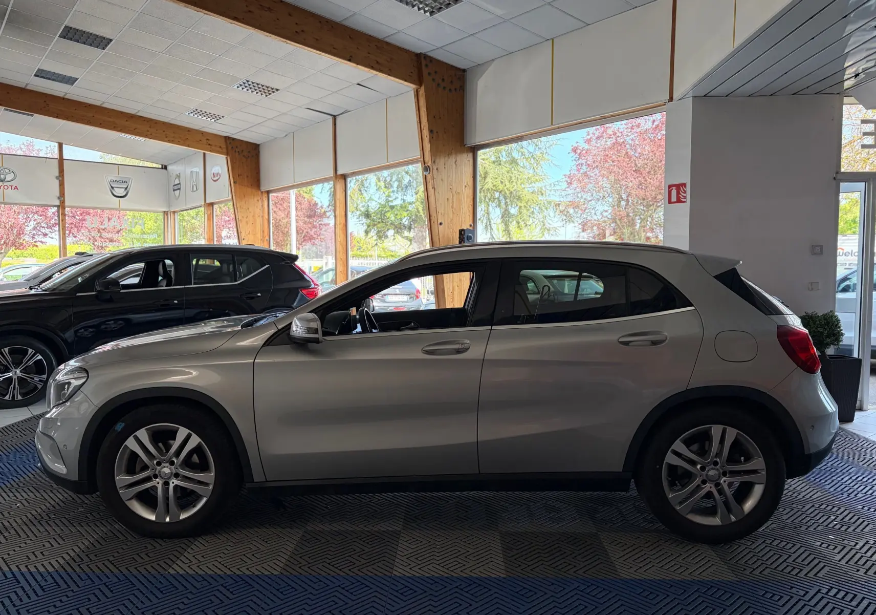 Vue de profil côté gauche d’un Mercedes GLA 200D Business gris exposé en showroom avec jantes alliage et intérieur visible.