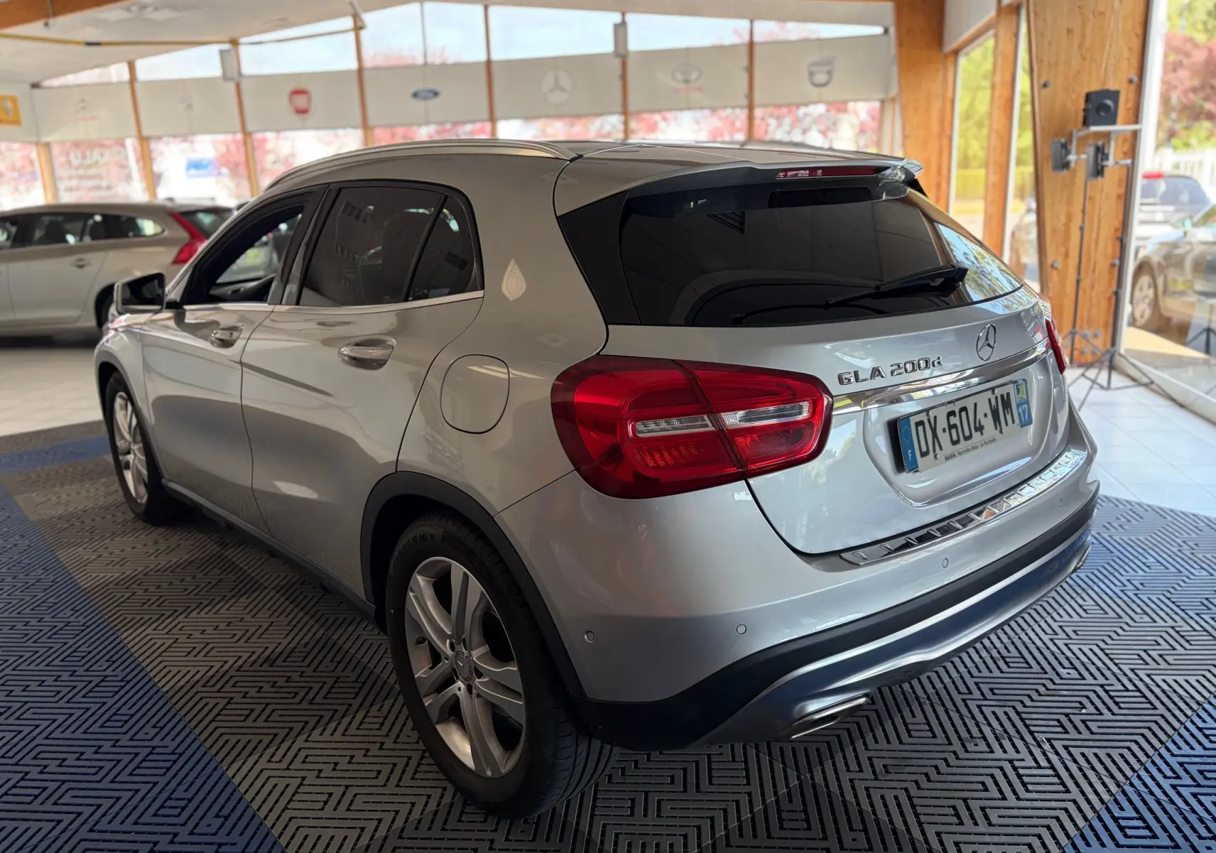 Vue 3/4 arrière droite d'une Mercedes GLA 200d Business gris métallisé, avec feux arrière LED et vitres teintées en showroom.