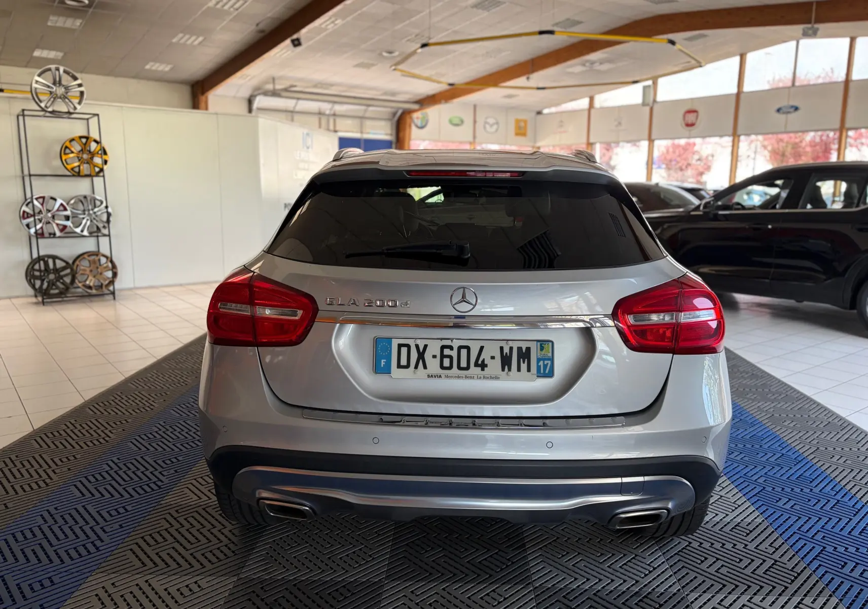 Vue arrière d'un Mercedes GLA 200D Business gris dans un showroom, avec feux rouges et double sortie d'échappement.