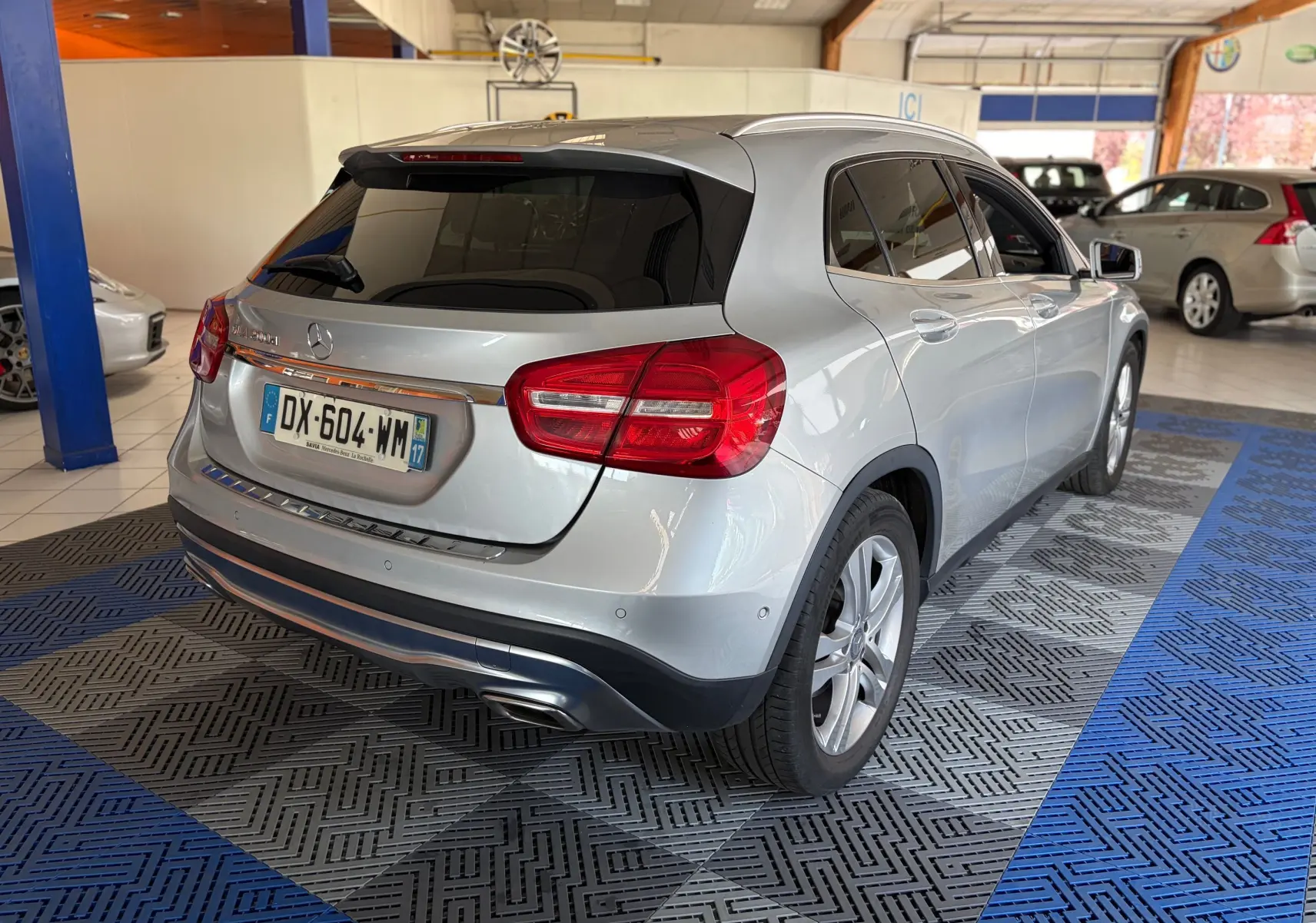Vue 3/4 arrière droite d’un Mercedes GLA 200D Business gris métallisé avec feux arrière rouges et vitres teintées, en intérieur showroom.