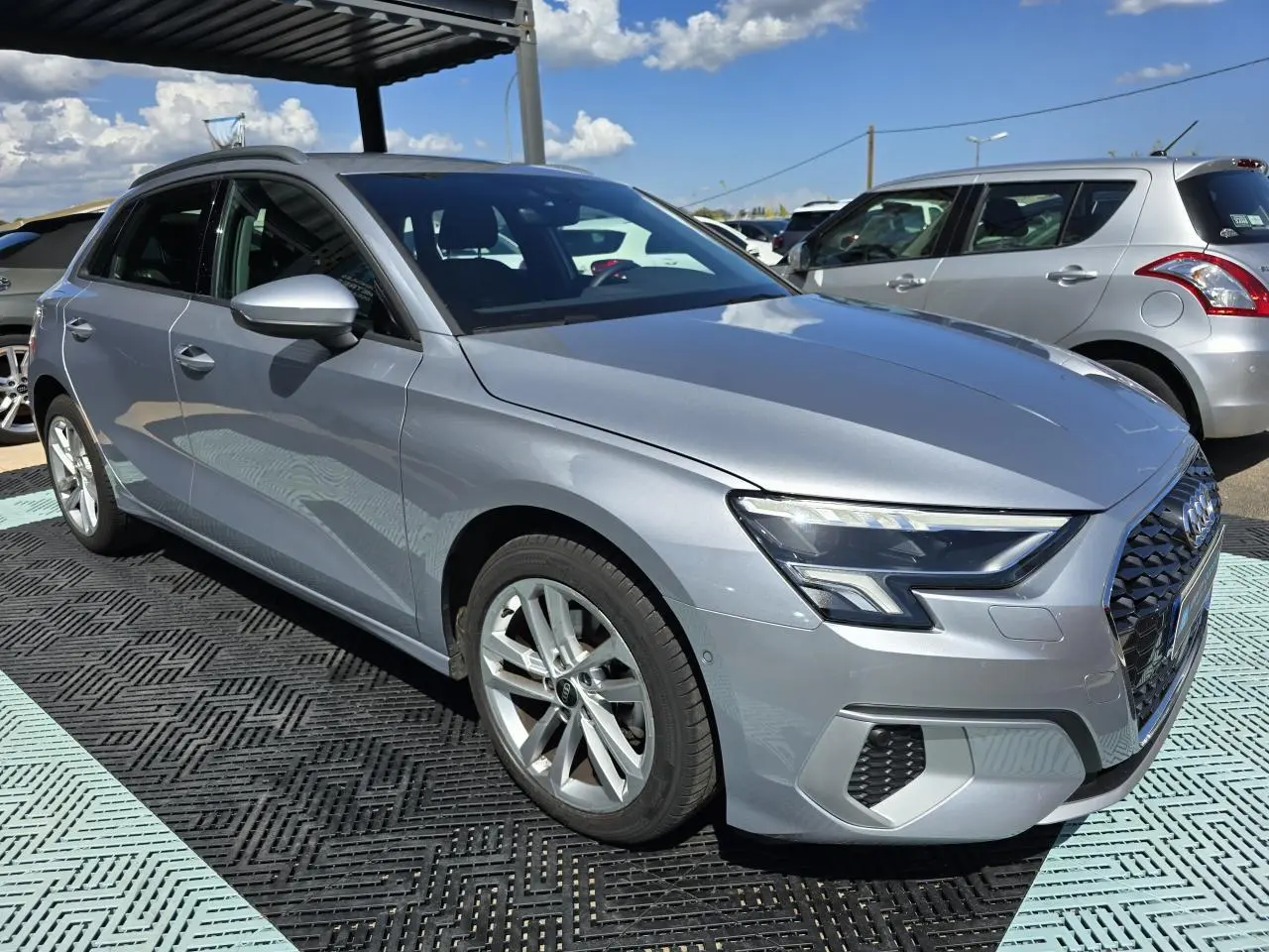 Audi A3 Sportback gris argent fleuret vue 3/4 avant droit, avec phares LED et jantes alliage 17 pouces.
