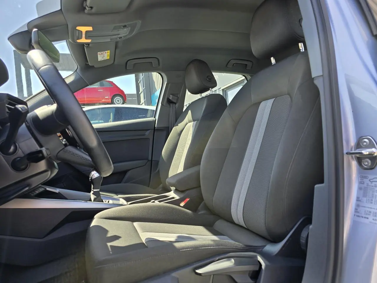 Vue intérieure côté conducteur de l'Audi A3 Sportback 2022, sièges gris avec bandes claires et volant cuir multifonctions.