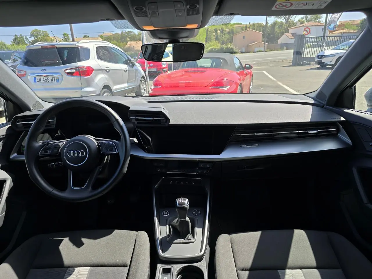 Vue intérieure avant de l'Audi A3 Sportback 2022 gris argent, volant cuir 3 branches et boîte manuelle visible.