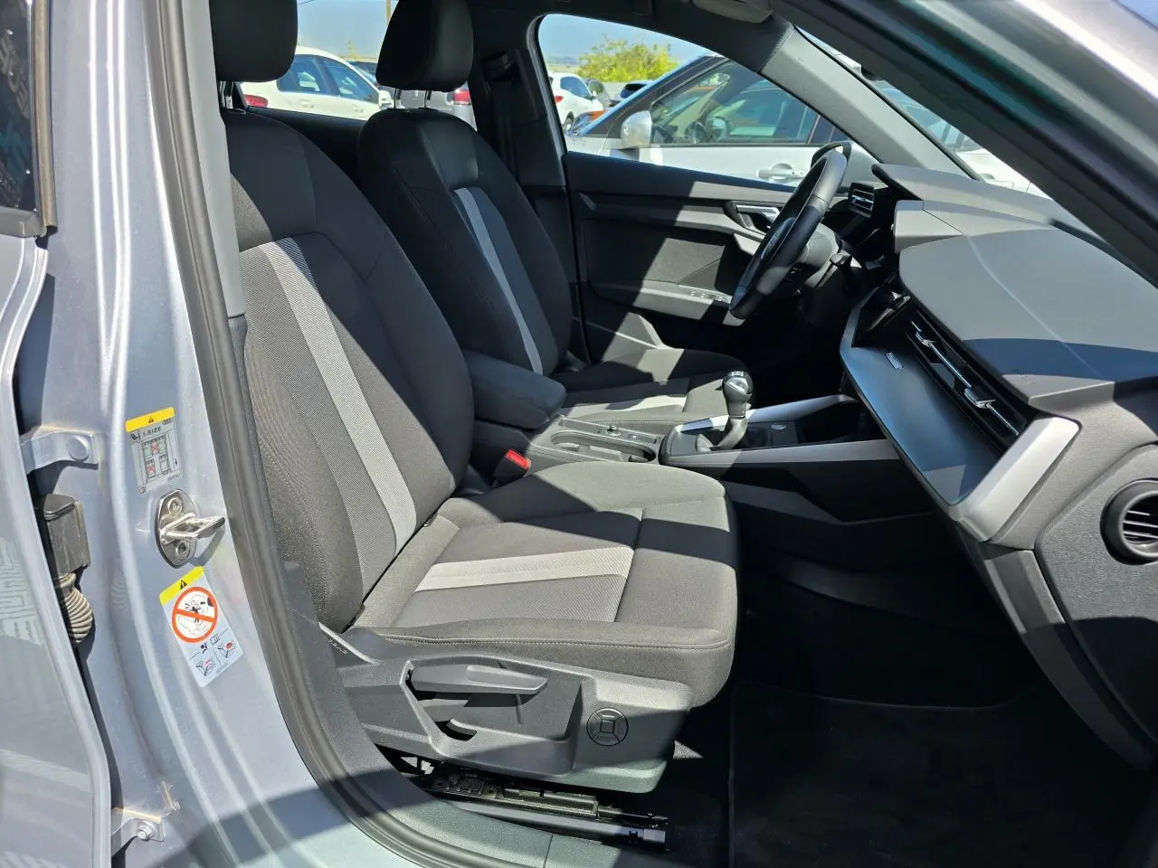 Vue intérieure côté conducteur de l'Audi A3 Sportback 2022 gris argent, avec sièges tissu bicolore et tableau de bord moderne.