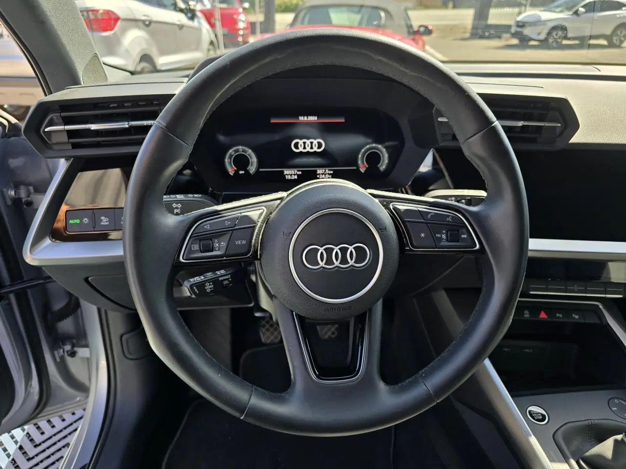 Vue intérieure centrée sur le volant cuir noir et l'Audi virtual cockpit d'une Audi A3 Sportback gris argent.