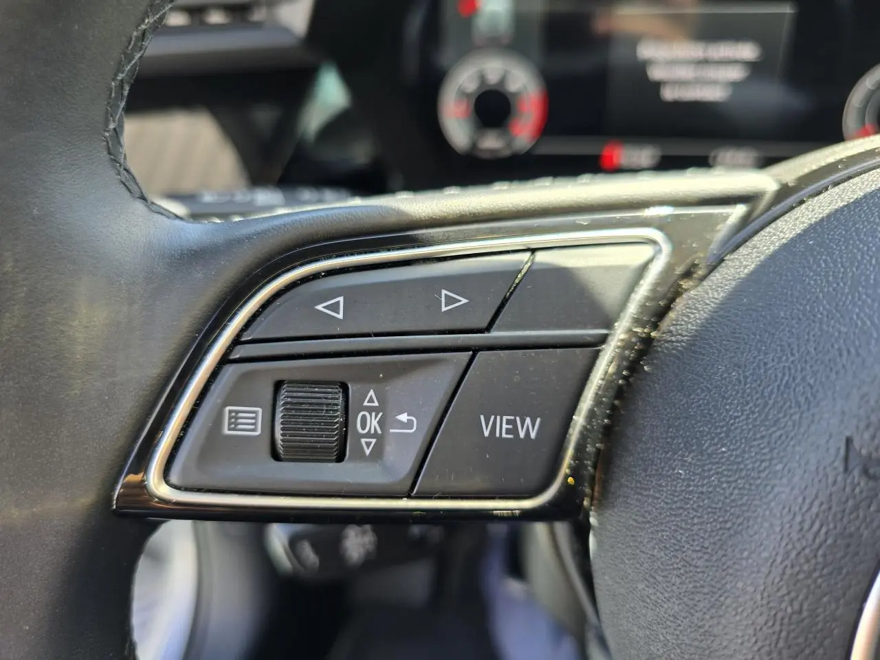 Gros plan sur les commandes gauche du volant cuir de l’Audi A3 Sportback gris argent, boutons de navigation et affichage.