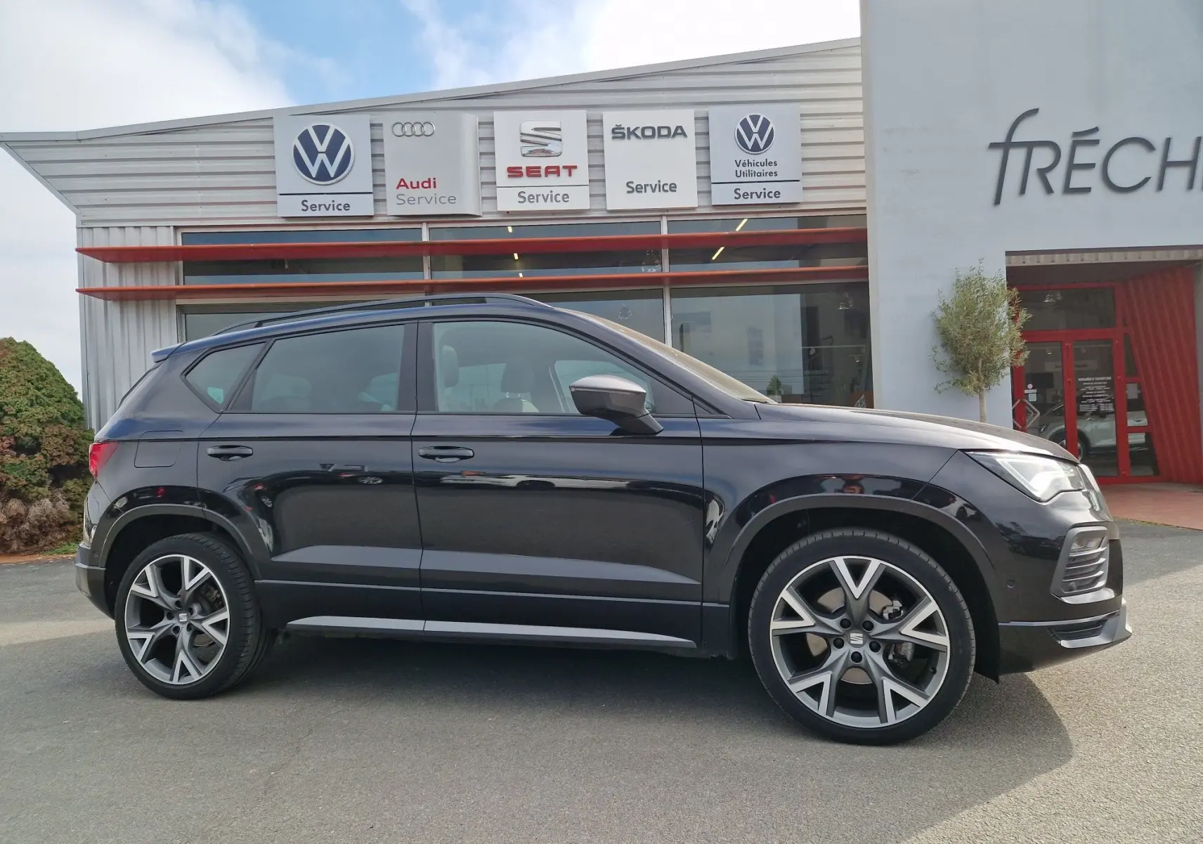 Vue de profil côté gauche d’un SEAT Ateca noir 2023 avec jantes alu 19 pouces, garé devant un service automobile.