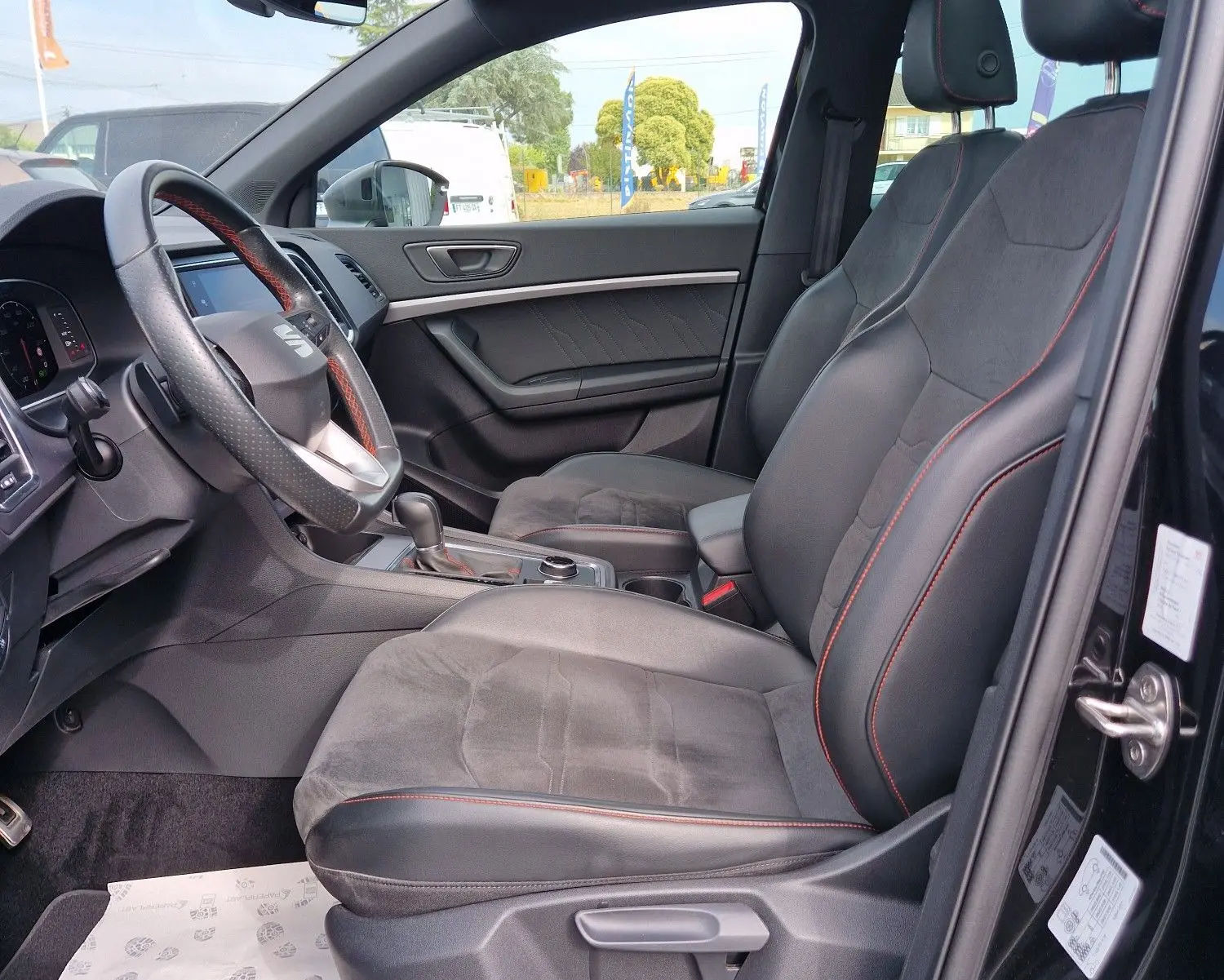 Vue intérieure côté conducteur du SEAT Ateca noir 2023, avec toit panoramique et sièges en cuir noir à surpiqûres rouges.