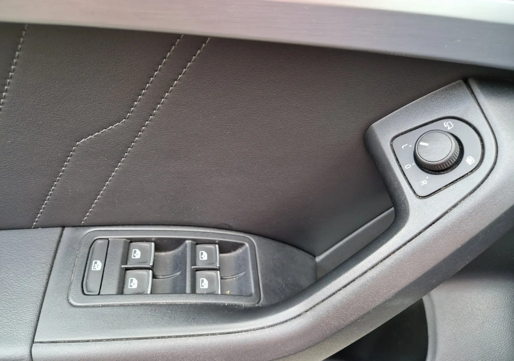 Gros plan sur la commande des vitres et réglage des rétroviseurs côté gauche intérieur d’un SEAT Ateca noir 2023.