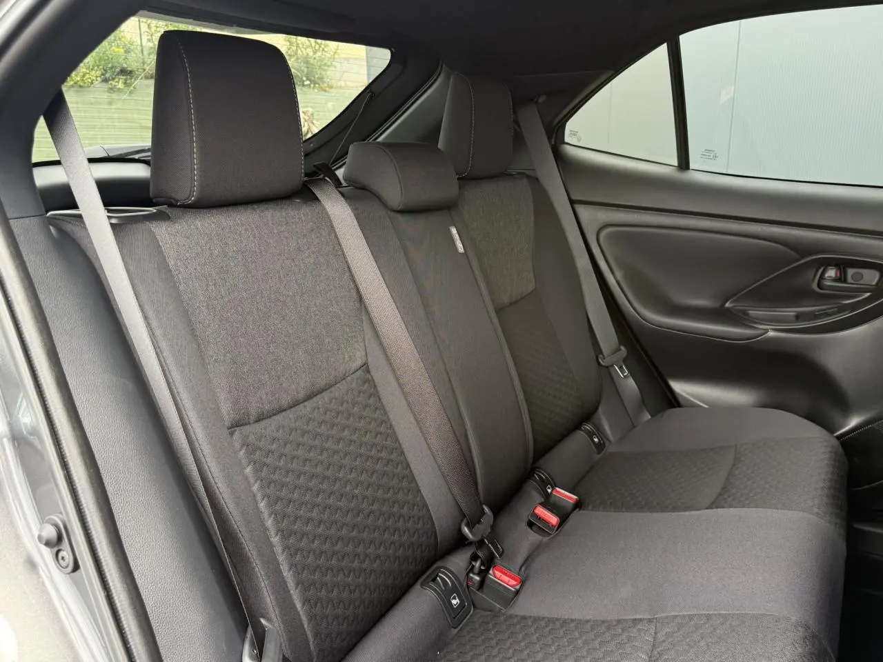 Vue latérale des sièges arrière gris foncé de la Toyota Yaris Cross 2026 avec ceinture de sécurité et porte noir mat.