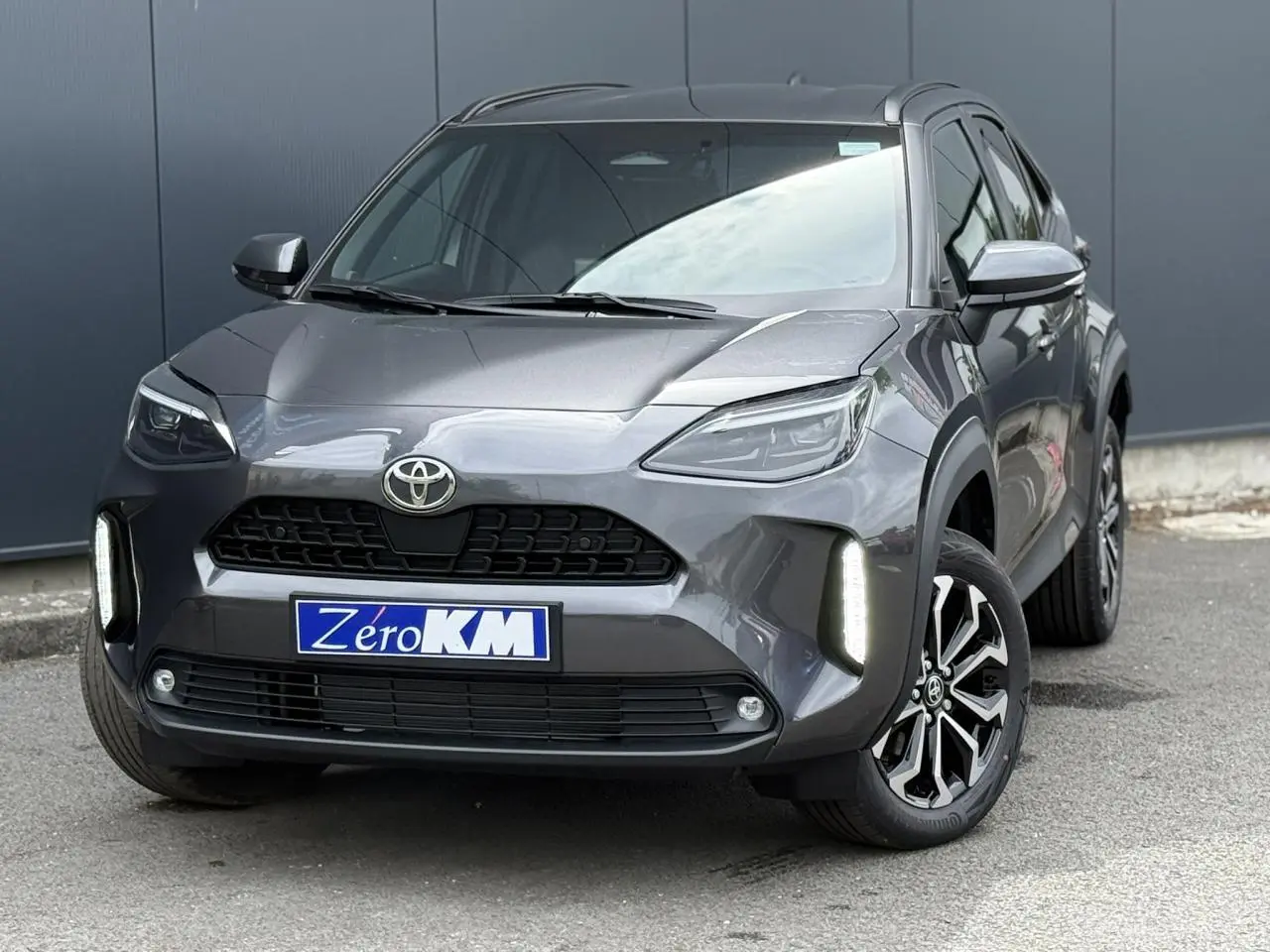 Toyota Yaris Cross gris Atlas vue 3/4 avant avec feux LED allumés et jantes alliage distinctives.