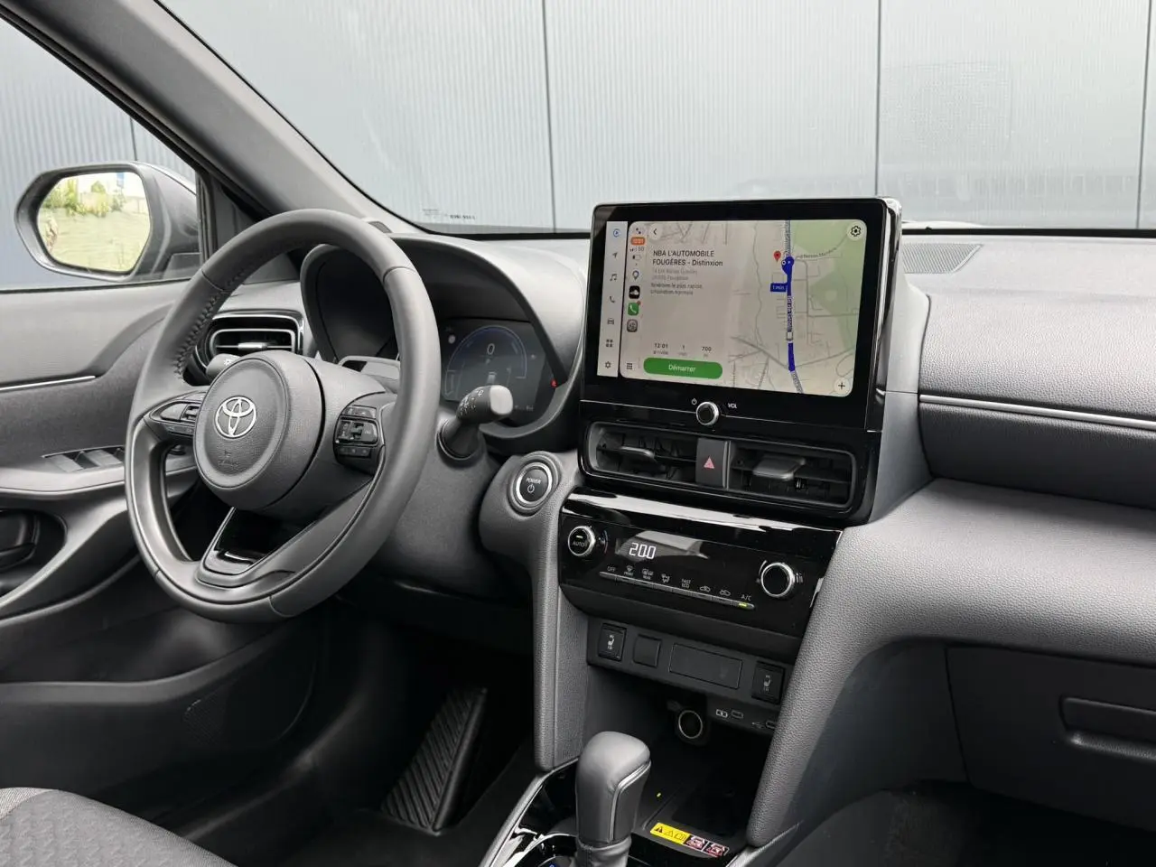 Vue intérieure avant droite du Toyota Yaris Cross gris Atlas 2026, avec écran tactile central et volant cuir.