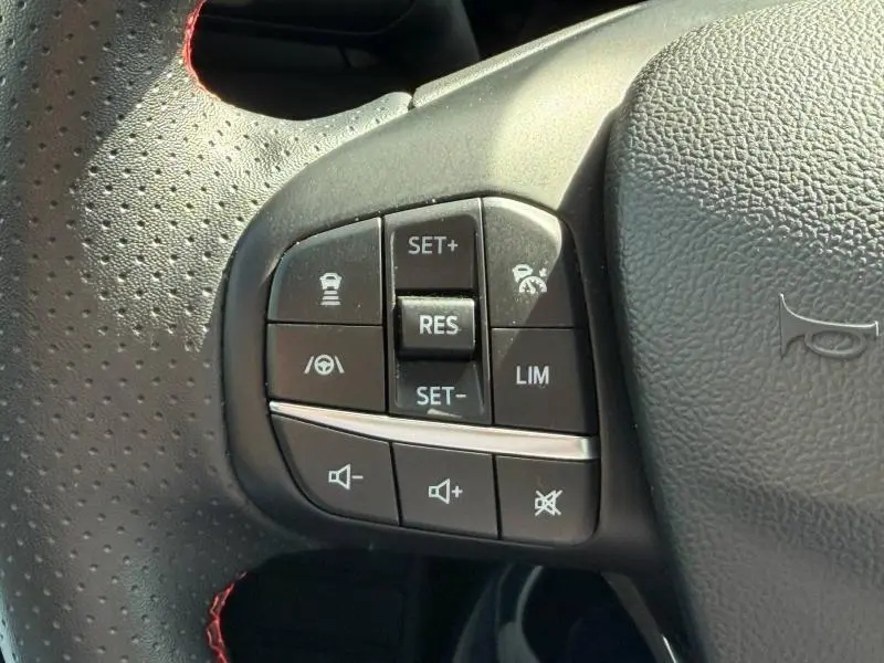 Gros plan sur les commandes multifonctions noires à gauche du volant cuir perforé gris d'une Ford Focus gris lunaire.