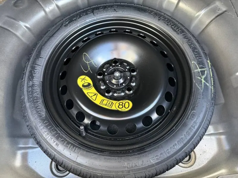 Pneu de secours noir avec étiquette jaune visible dans le coffre d'une Ford Focus gris lunaire métallisé.
