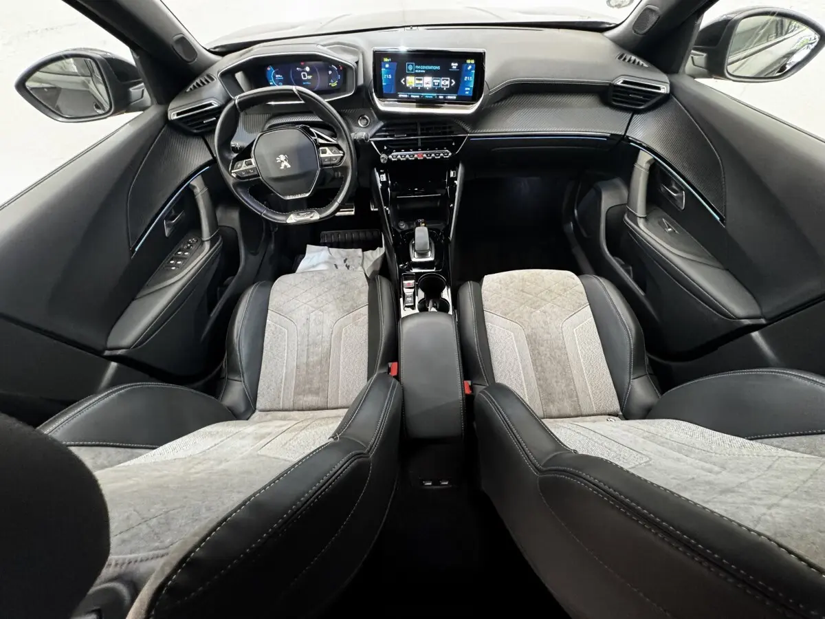 Vue intérieure avant du Peugeot E-2008 électrique GT Pack 2021, avec sièges bi-matière gris et noir et tableau de bord numérique.