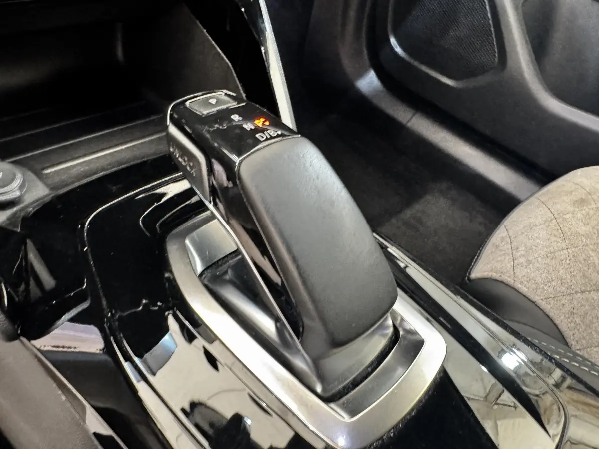 Gros plan sur la commande de boîte automatique noire brillante du Peugeot E-2008 électrique GT Pack, intérieur tissu gris.