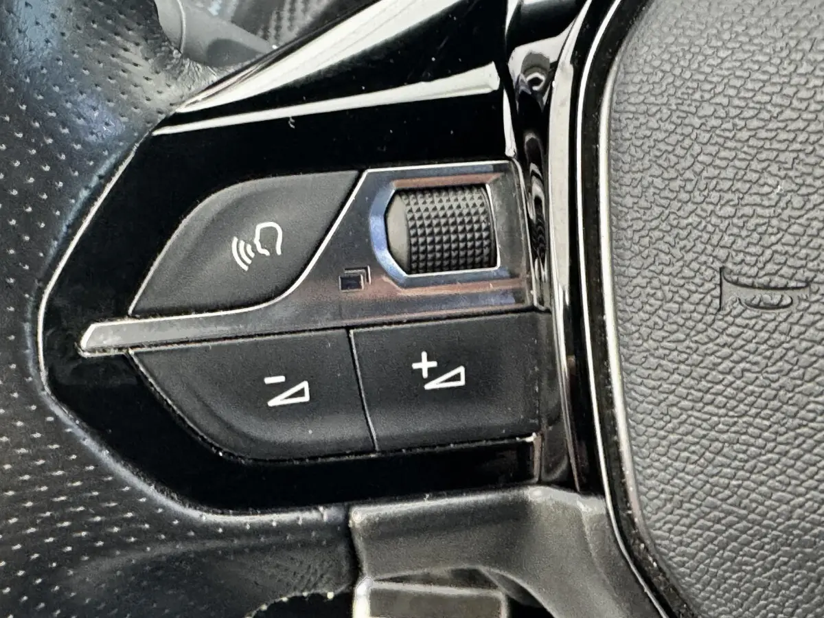 Gros plan sur les commandes multifonctions du volant cuir noir du Peugeot E-2008 électrique GT Pack 2021.