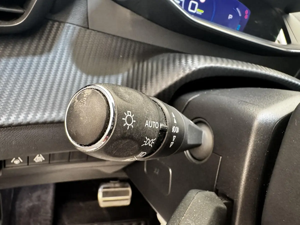 Gros plan sur la commande d’éclairage noire à gauche du volant dans l’habitacle du Peugeot E-2008 électrique noir.