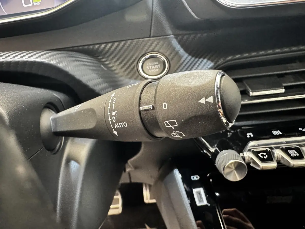 Gros plan sur la commande d’essuie-glace à gauche du volant cuir dans l’habitacle noir du Peugeot E-2008 électrique GT Pack.