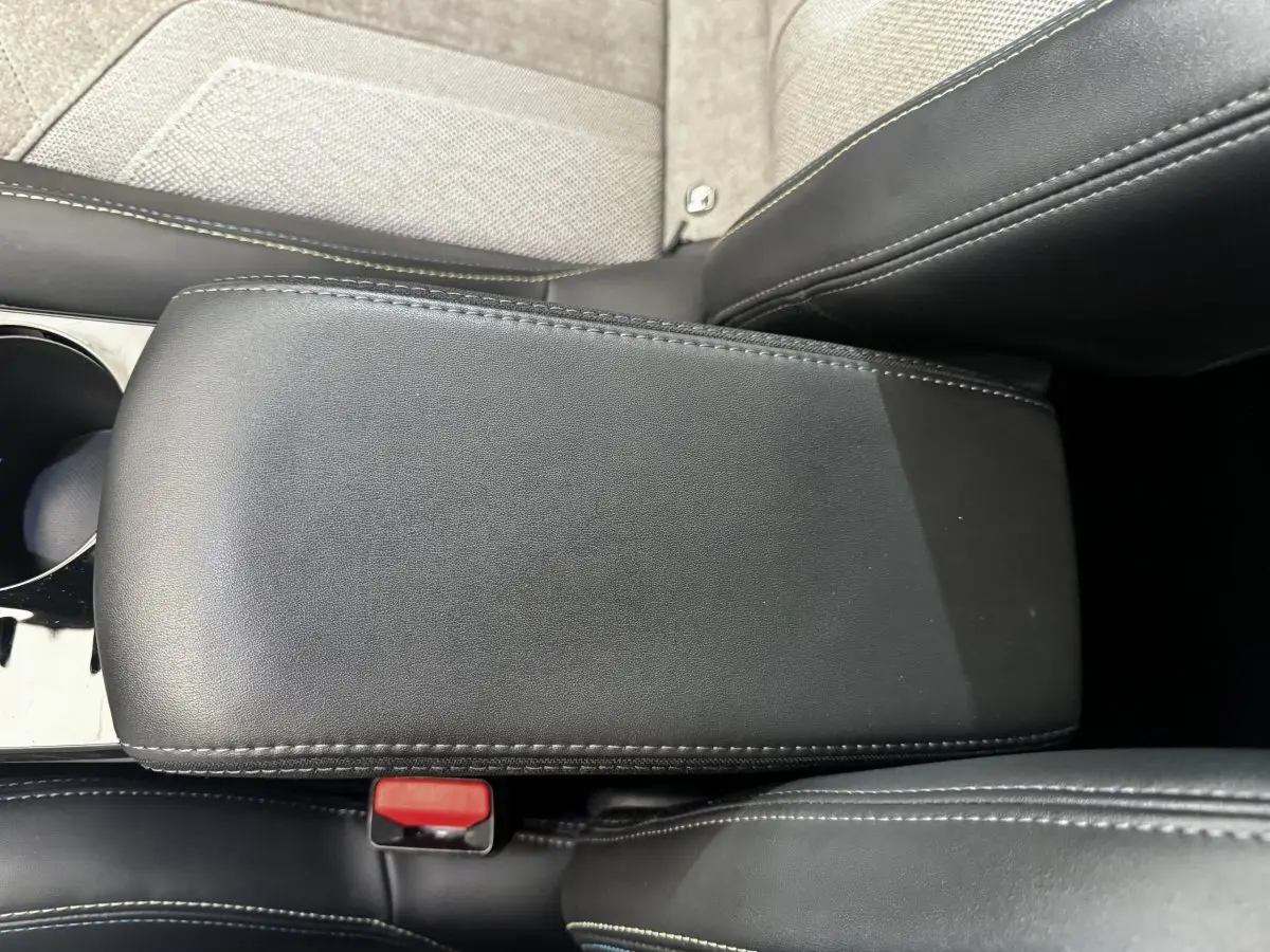 Gros plan sur l'accoudoir central en cuir noir avec surpiqûres blanches dans l'habitacle du Peugeot E-2008 électrique.