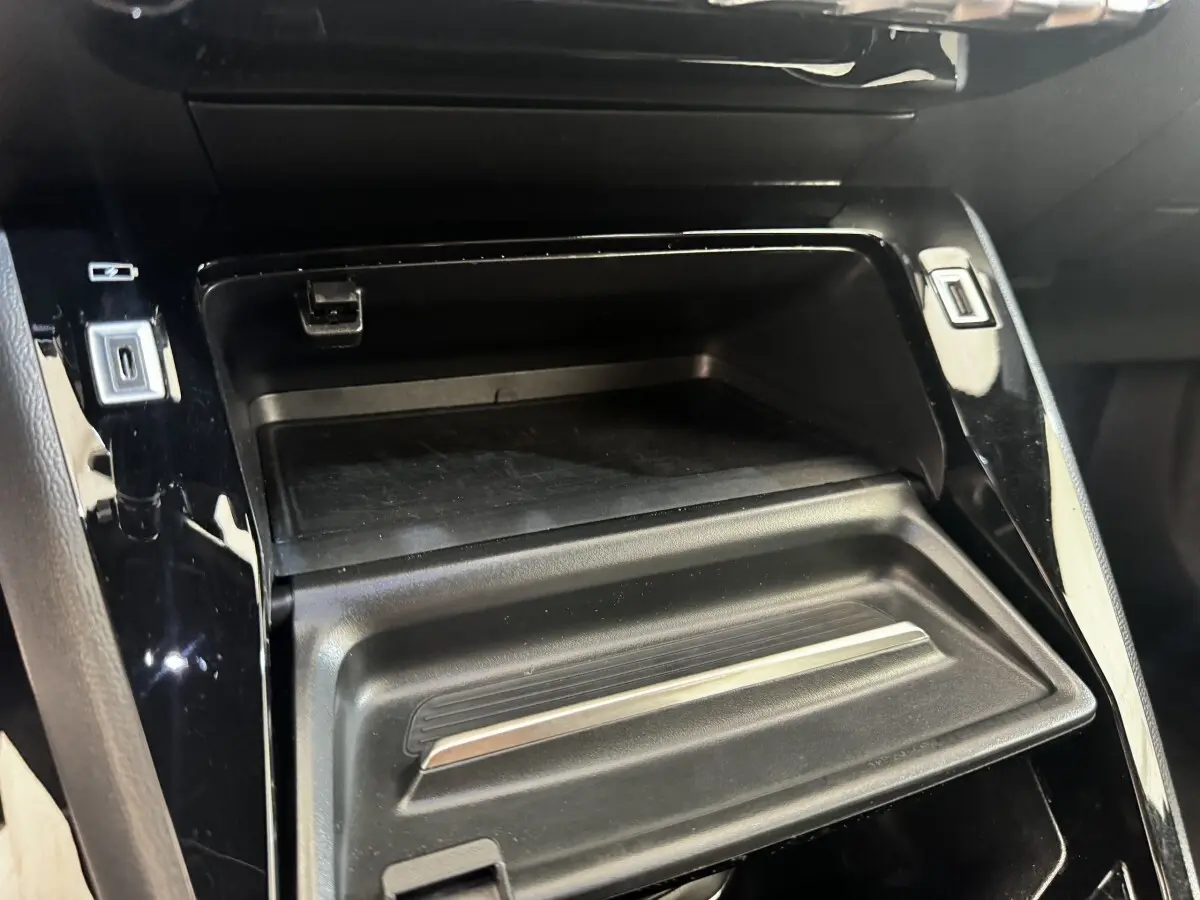 Gros plan sur le rangement central noir brillant du Peugeot E-2008 électrique GT Pack 2021, avec ports USB visibles.