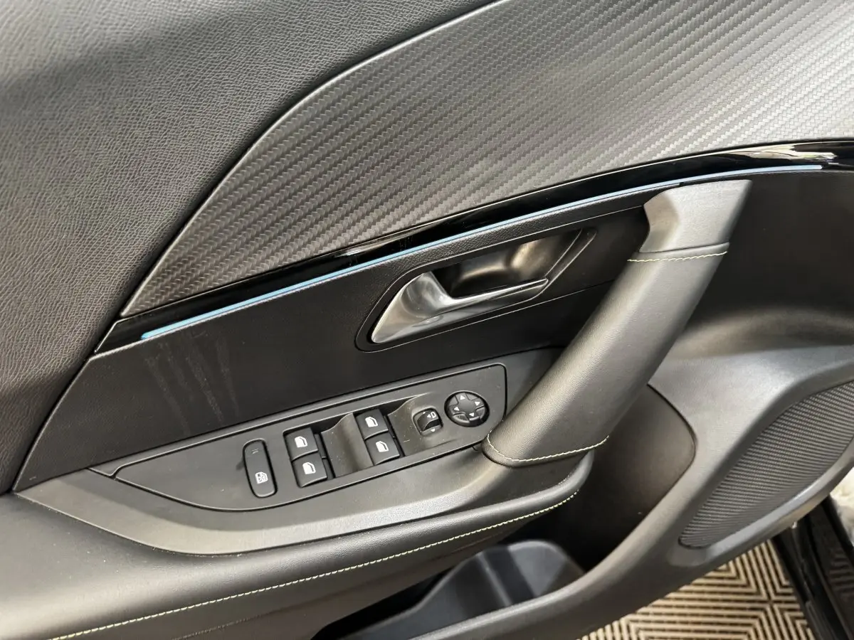 Gros plan sur la porte intérieure côté gauche noire du Peugeot E-2008 électrique GT Pack avec commandes de vitres et poignée cuir.