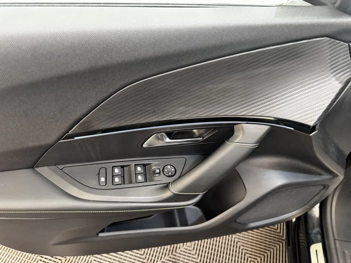 Vue intérieure côté gauche de la porte PEUGEOT E-2008 GT Pack noire avec commandes vitres et insert effet carbone.