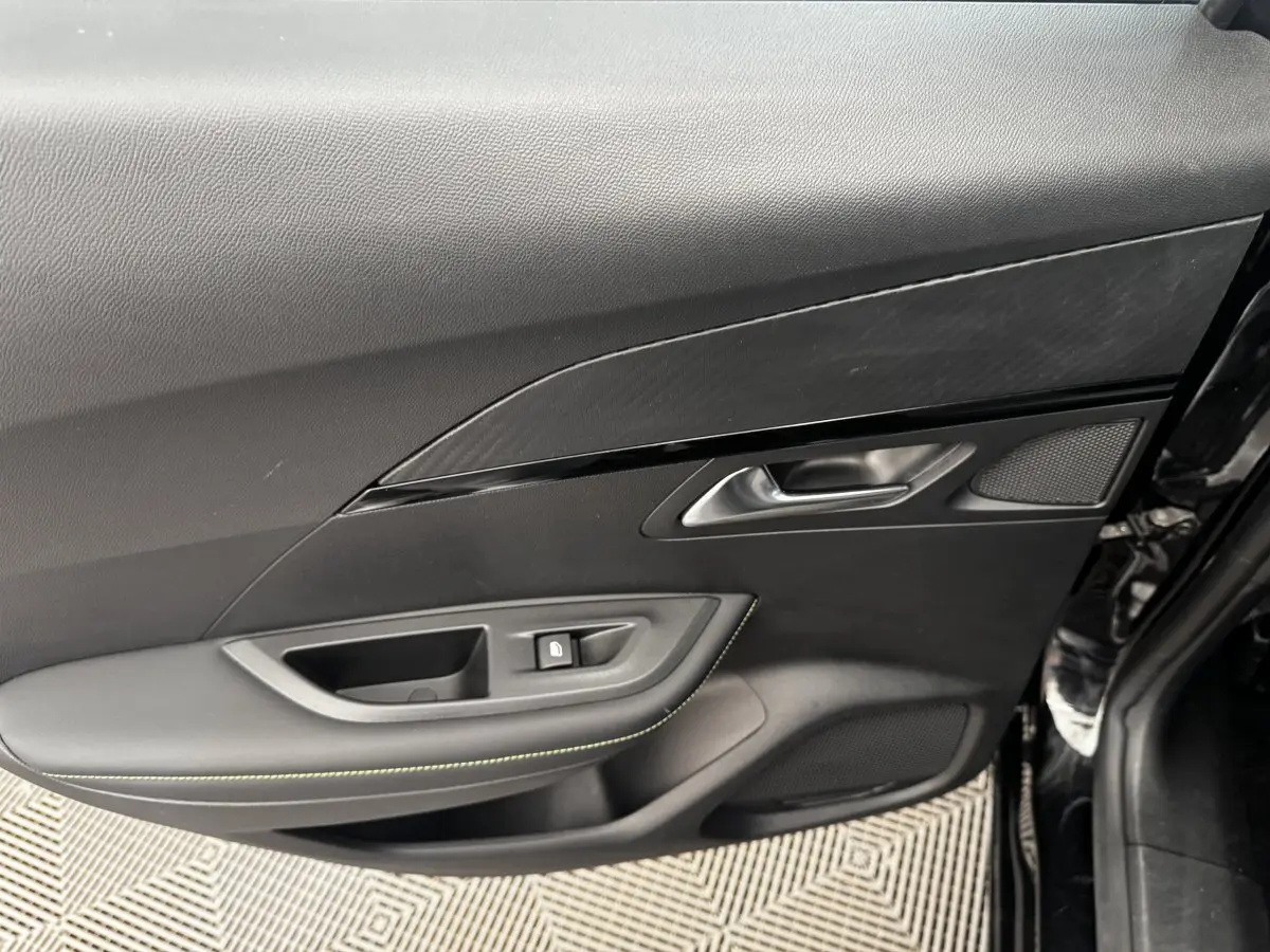 Détail de la porte intérieure côté gauche du Peugeot E-2008 électrique GT Pack noir, avec poignée et bouton de verrouillage.