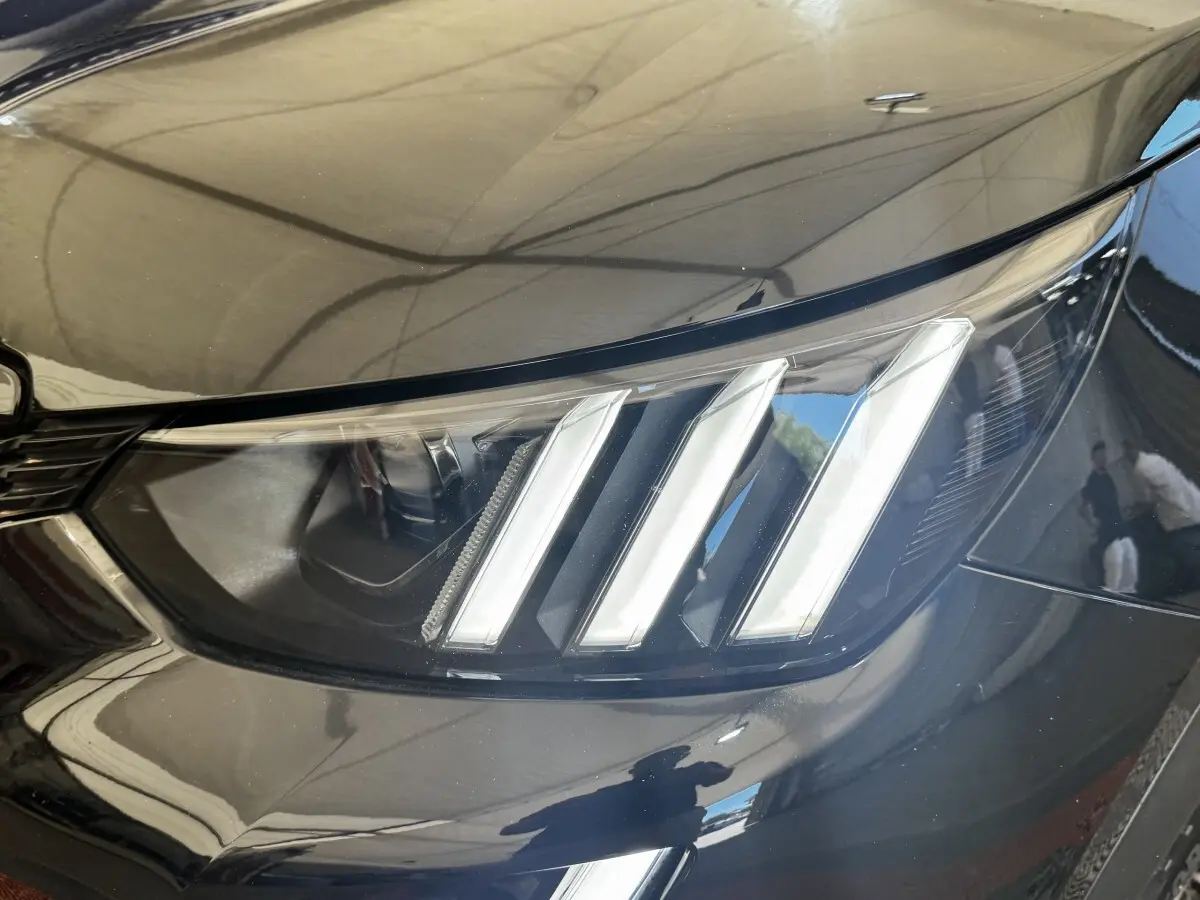 Gros plan sur le phare avant droit noir brillant du Peugeot E-2008 électrique GT Pack 2021 avec signature lumineuse à trois griffes.