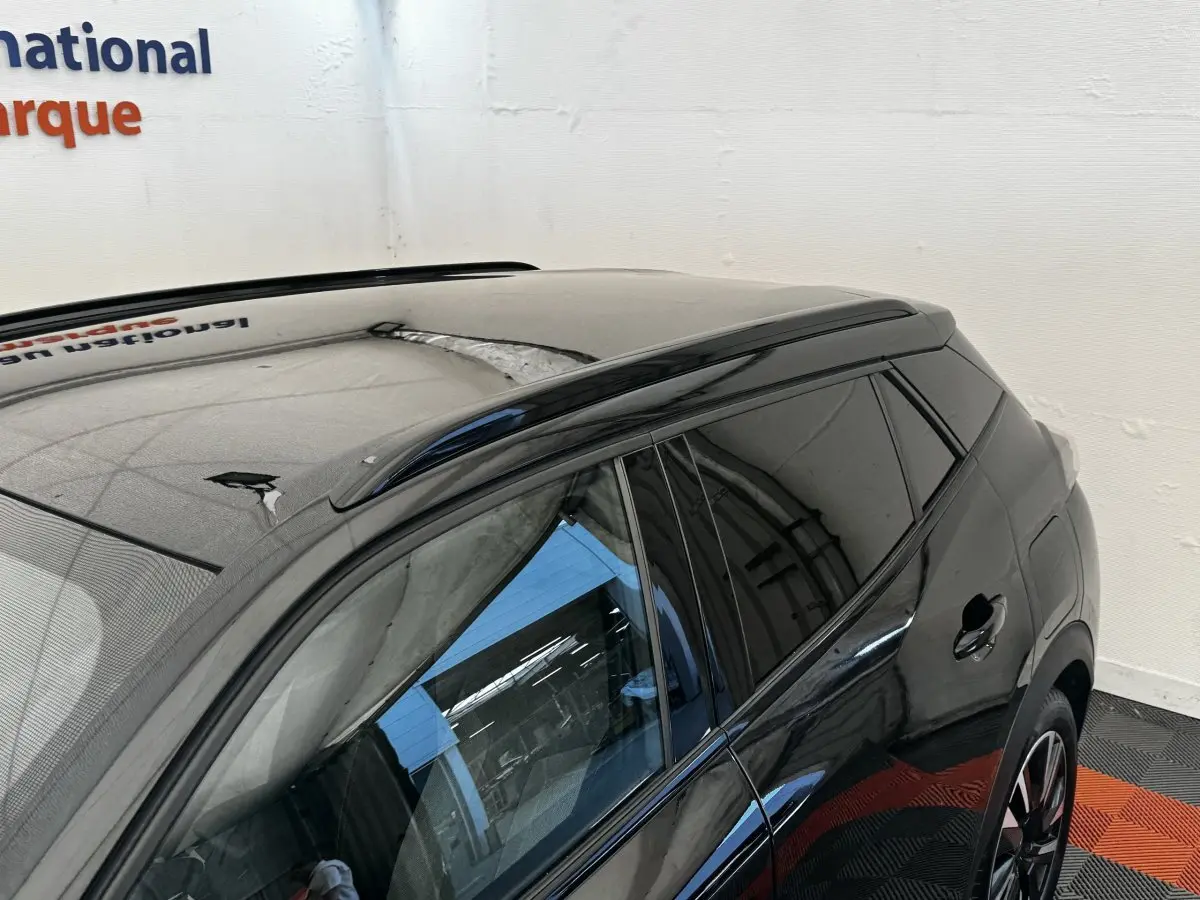 Vue 3/4 arrière côté gauche d’un Peugeot E-2008 électrique GT Pack noir avec vitres teintées et barres de toit noires.