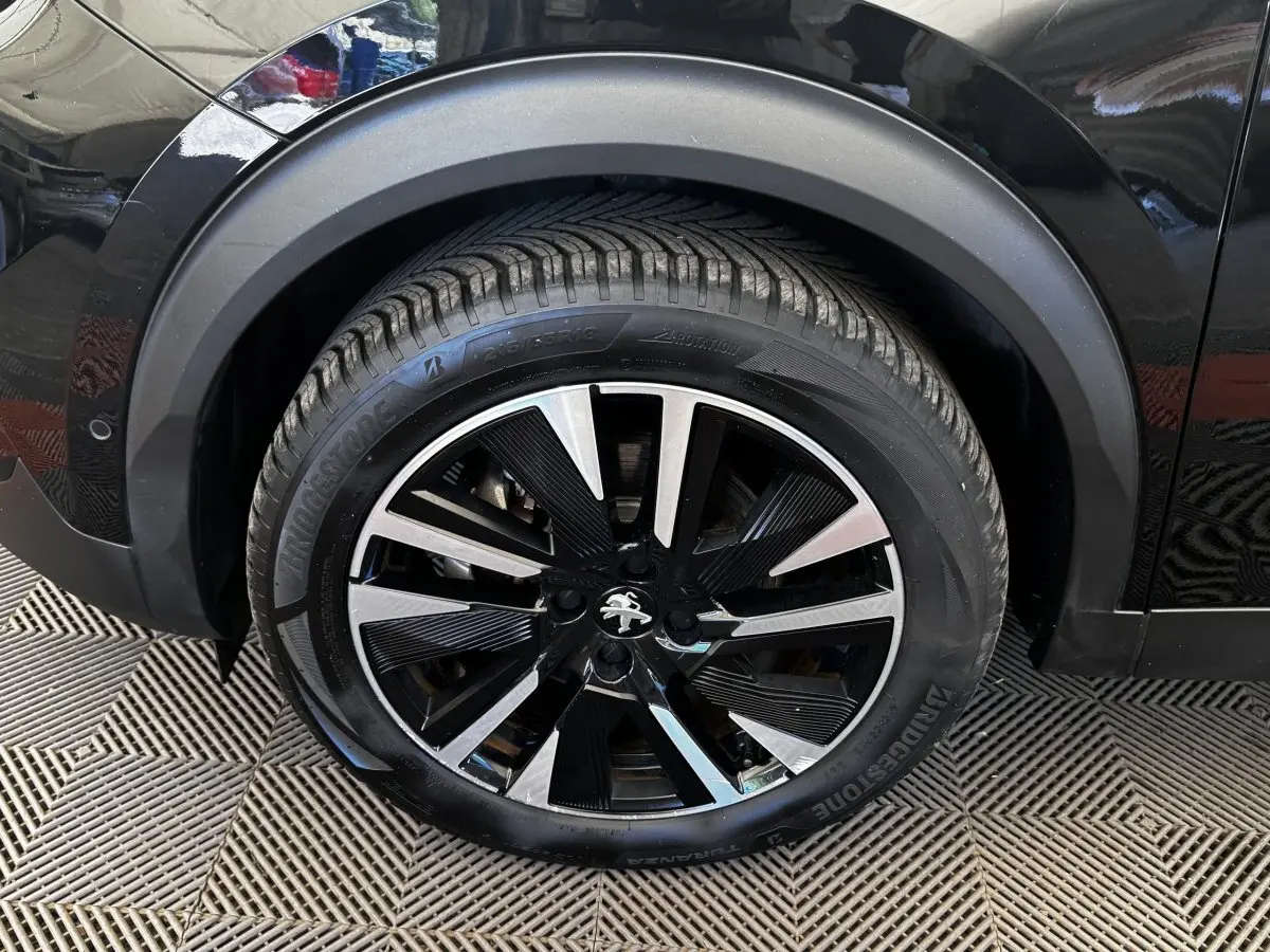Gros plan sur la roue avant gauche noire du Peugeot E-2008 électrique GT Pack avec jante alliage bicolore.