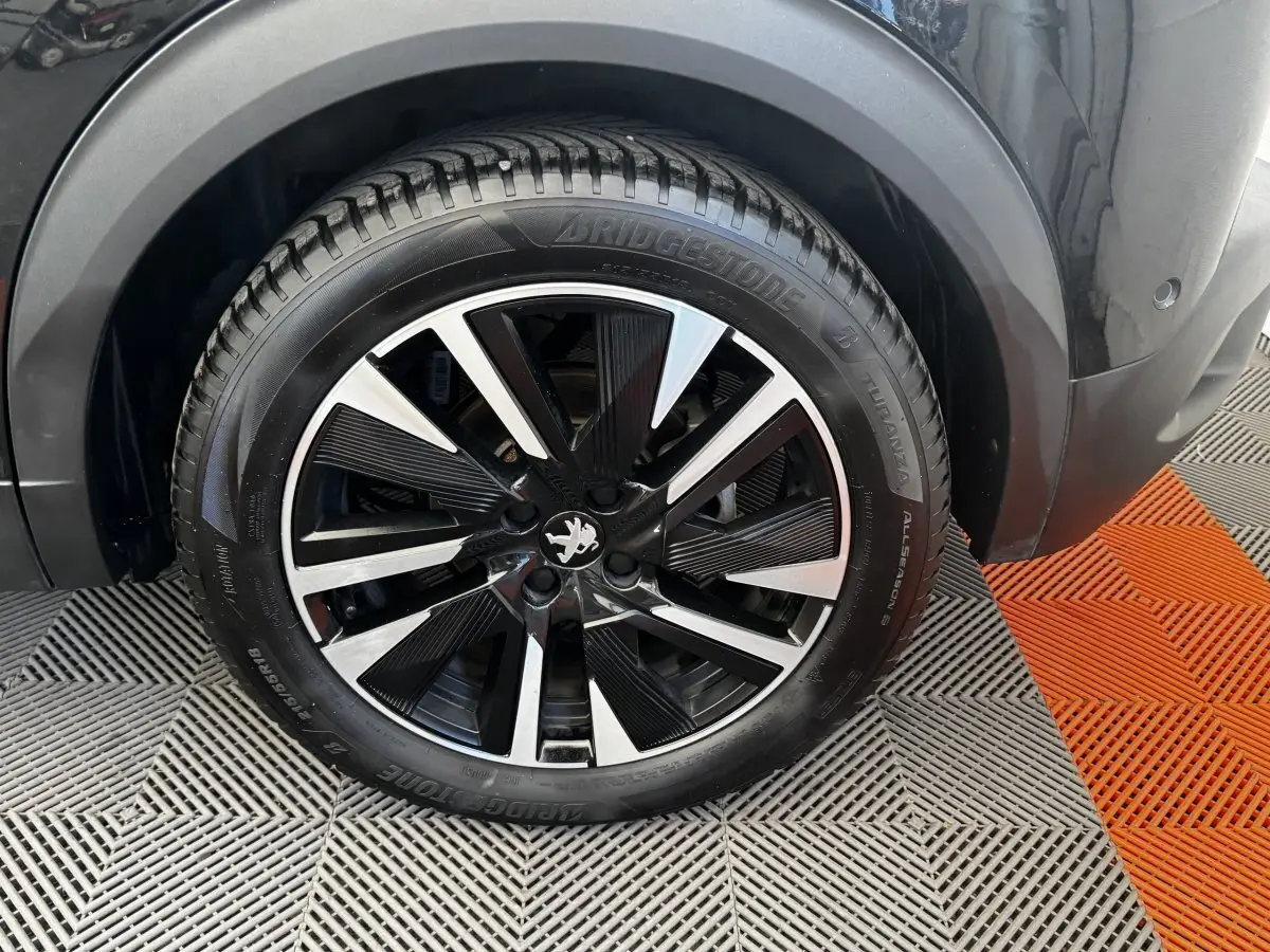 Gros plan sur la roue avant droite noire du Peugeot E-2008 électrique GT Pack avec jante alliage bicolore.