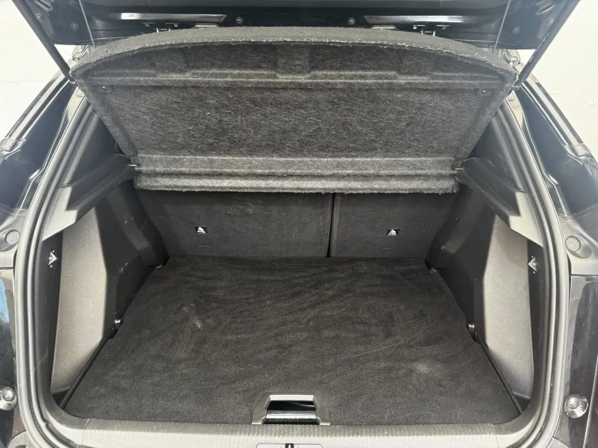 Coffre ouvert vu de l'arrière d'un Peugeot E-2008 électrique GT Pack noir, espace de rangement vide et tapis noir.