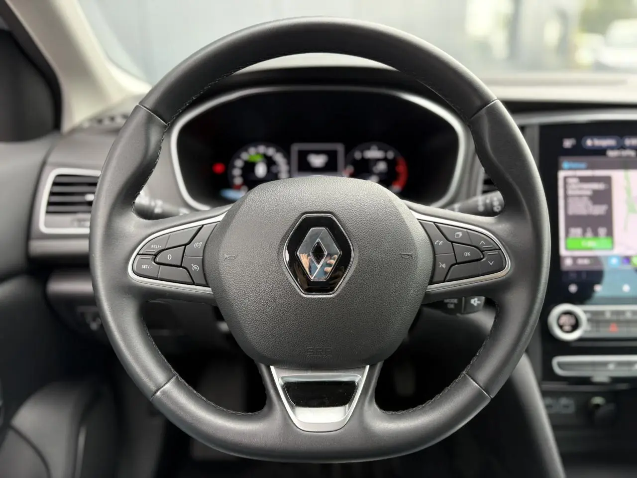 Volant en similicuir noir avec logo Renault au centre, tableau de bord numérique et écran tactile GPS à droite.